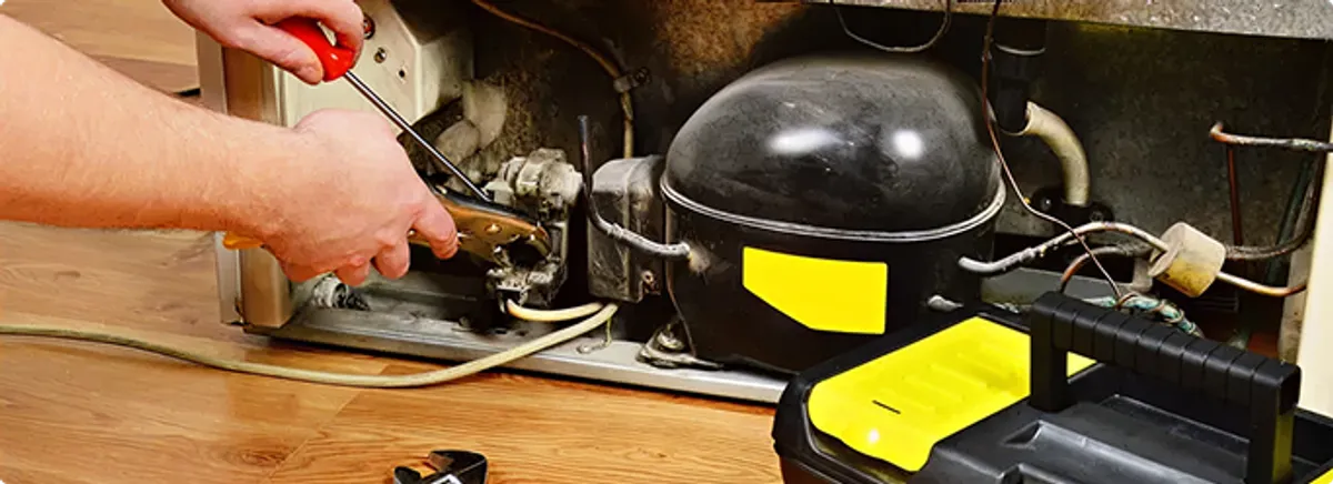 Refrigerator repair technician fixing the compressor and wiring in Keene, CA