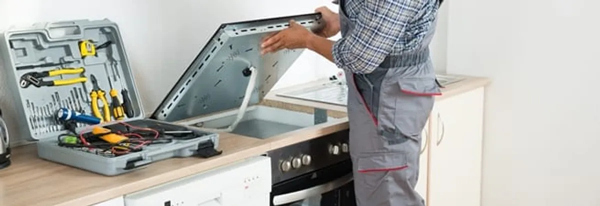 Cooktop repair technician lifting a built-in stovetop for service in Bakersfield, CA
