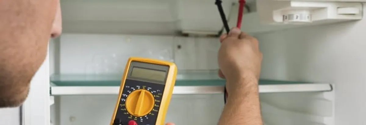 Refrigerator repair technician testing electrical components with a multimeter in Bakersfield, CA