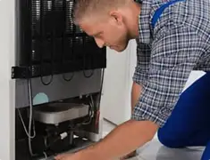 Refrigerator repair technician servicing the compressor and condenser area in Bakersfield, CA